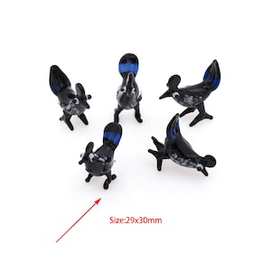 May include: Five black and blue glass bird figurines. Each bird is approximately 29x30mm in size. The birds are standing on a white surface.