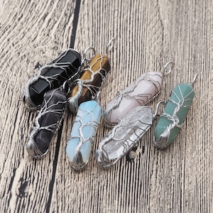 Puede incluir: Un conjunto de siete colgantes de cristal envueltos en alambre. Los cristales son de varios colores, incluyendo negro, marrón, dorado, rosa, transparente, azul y verde. El alambre envuelto crea un diseño de árbol.