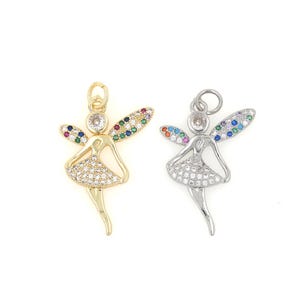 May include: Two gold and silver charm pendants in the shape of a fairy with wings and a dress decorated with colorful and clear rhinestones.