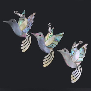 May include: Three iridescent hummingbird pendants made of mother of pearl. The hummingbirds are in flight with their wings spread. The pendants are a light blue colour with iridescent green, blue, and purple accents.