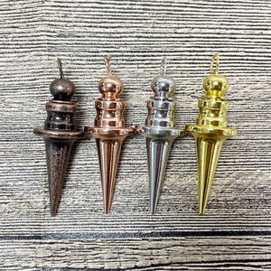 Pode incluir: Quatro pêndulos de metal com diferentes acabamentos: bronze, cobre, prata e ouro. Cada pêndulo tem uma ponta pontiaguda e uma parte superior redonda.