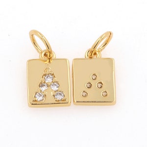 Peut inclure: Deux breloques dor&eacute;es de forme carr&eacute;e avec une boucle pour les attacher &agrave; un collier ou un bracelet. Un charme a la lettre A faite de strass clairs, l'autre charme a une forme triangulaire faite de strass clairs.