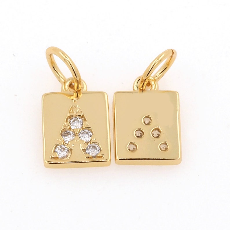 Peut inclure: Deux breloques dor&eacute;es de forme carr&eacute;e avec une boucle pour les attacher &agrave; un collier ou un bracelet. Un charme a la lettre A faite de strass clairs, l'autre charme a une forme triangulaire faite de strass clairs.