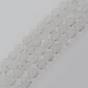 Puede incluir: Una hebra de cuentas de cristal transparente con un diseño facetado y acanalado. Las cuentas son redondas y tienen un acabado liso y pulido.