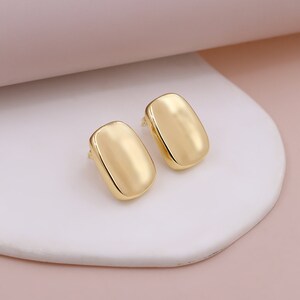 May include: A pair of gold-toned rectangle shaped earrings. The earrings are smooth and have a shiny finish.