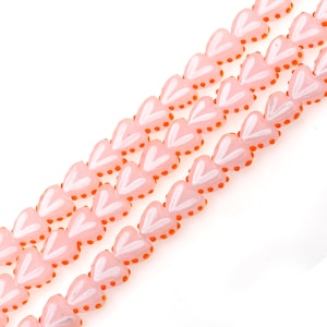 May include: A strand of pink heart-shaped glass beads with white and orange accents. The beads are strung together on a clear thread.