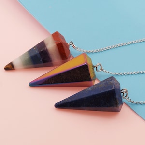 May include: Three crystal pendulums with chains. The pendulums are made of different types of crystals: a multi-colored crystal, a rainbow iridescent crystal, and a blue crystal.