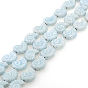 Op de afbeelding: Een streng lichtblauwe keramische kralen in de vorm van schelpen. Elke kraal heeft een gedetailleerd spiraalontwerp.