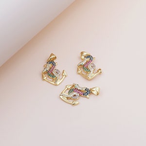 Könnte beinhalten: Drei goldene Anker-Anhänger mit bunten Zirkonia-Steinen. Die Anker sind mit einem Seil-Design verziert und haben eine Öse oben zum Anbringen an einer Kette oder einem Armband.
