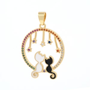 May include: Gold pendant necklace featuring two black and white cats sitting under a circle of colorful gemstones. The circle has a design of stars hanging from it.