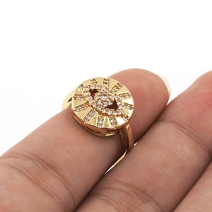 May include: A gold ring with a round, eye-shaped design set with clear cubic zirconia stones.