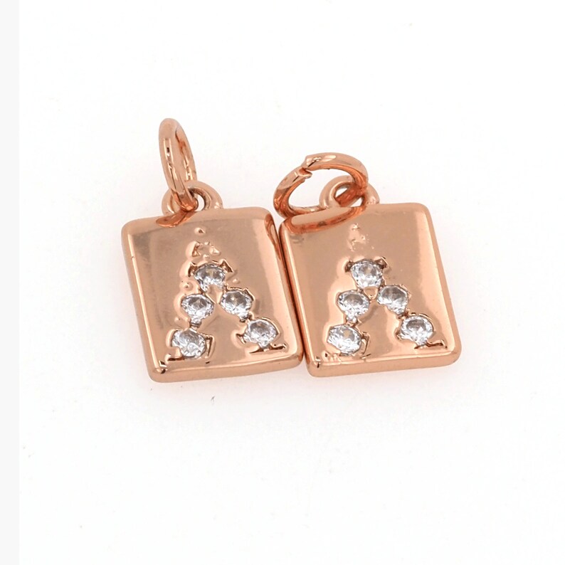 Peut inclure: Deux breloques dor&eacute;es avec la lettre "A" en strass transparents. Chaque breloque est de forme carr&eacute;e avec une boucle en haut pour l'attacher &agrave; un bracelet ou un collier.