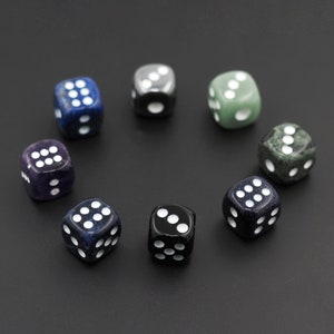 May include: Eight dice of different colors and patterns, including black, green, blue, and purple, arranged in a circle on a black surface.