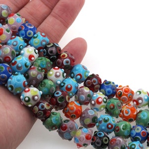 May include: A strand of colorful glass beads with a textured, bumpy surface. Each bead is decorated with a variety of small, colorful circles.