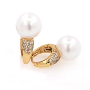 May include: A pair of gold hoop earrings with a large white pearl on each hoop. The hoops are encrusted with small clear stones.