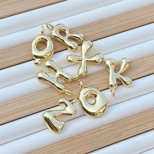 Puede incluir: Un conjunto de seis abalorios de letras de metal de color dorado en una fuente de burbujas. Las letras son O, R, X, K, H y Z.