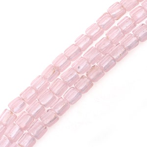 Könnte beinhalten: Drei Stränge hellrosa, rechteckiger Perlen. Jede Perle hat eine leicht abgerundete Form mit vertikalen Rillen. Die Perlen sind aufgereiht und erzeugen eine zarte Ästhetik. Der Hintergrund ist weiß.