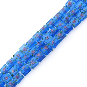 May include: A strand of blue glass beads with a floral pattern. The beads are rectangular and have a translucent appearance. The flowers are pink and green.