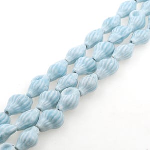 May include: A strand of light blue ceramic beads with a ribbed texture. The beads are shaped like teardrops or small gourds.