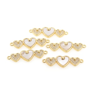 May include: Five gold-tone heart-shaped connectors with clear rhinestones and a white mother-of-pearl center. Each connector has two loops for attaching to jewelry.