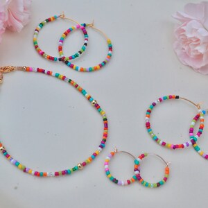May include: A set of colorful beaded jewelry, including a necklace, a pair of earrings, and a bracelet. The beads are multi-colored and arranged in a random pattern. The jewelry is made with gold-toned metal.