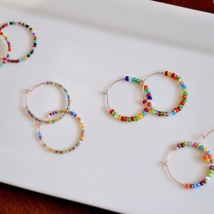 May include: Four pairs of colorful beaded hoop earrings. The earrings are made with small, multi-colored beads and are available in a variety of sizes.