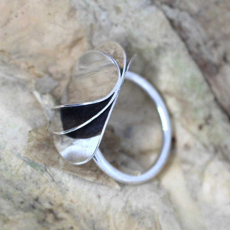 K&ouml;nnte beinhalten: Ein silberner Ring mit einem einzigartigen Design, das aus mehreren &uuml;berlappenden, gekr&uuml;mmten Formen besteht, die Bl&uuml;tenbl&auml;ttern &auml;hneln.