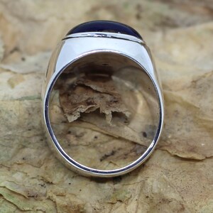 K&ouml;nnte beinhalten: Ein silberner Ring mit einem dunkelblauen ovalen Edelstein, der in einer Zargenfassung sitzt.