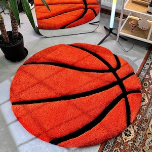 May include: Orange and black round rug shaped like a basketball. The rug is made of a soft, fluffy material.