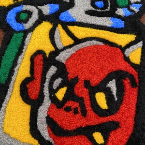 K&ouml;nnte beinhalten: Ein farbenfroher, abstrakter Teppich mit einem cartoonartigen Charakter. Das Design umfasst ein rotes Gesicht, gelbe Augen und schwarze Umrisse sowie gelbe, blaue, gr&uuml;ne und graue Elemente. Der Teppich hat einen strukturierten, getufteten Look.