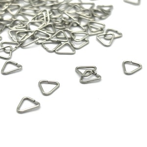 May include: A pile of silver triangle-shaped metal rings, with a few scattered on a white surface.