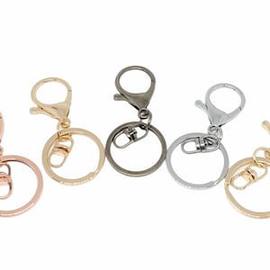 May include: Five keychains with different metal finishes: rose gold, antique brass, silver, and gold. Each keychain has a round ring and a lobster claw clasp.
