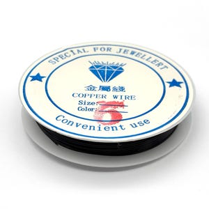 May include: A spool of dark-colored copper wire for jewelry making. The white circular label features a blue diamond icon, two stars, and the text: SPECIAL FOR JEWELLERY, COPPER WIRE, Convenient use, and a large red number 6 printed in the center.