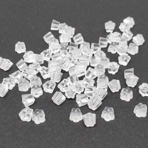May include: A large pile of clear plastic earring backs. The backs are shaped like a flower with a small, round center.
