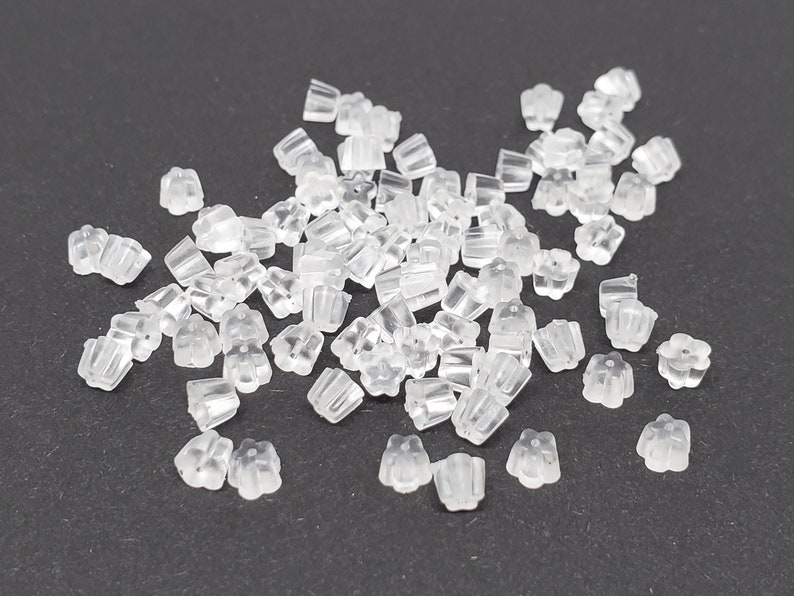 May include: A large pile of clear plastic earring backs. The backs are shaped like a flower with a small, round center.
