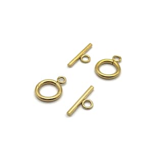 May include: Four gold-coloured toggle clasps, suitable for jewellery making. The clasps consist of a circular ring with a small loop and a straight bar with a loop. The clasps are shown against a white background.
