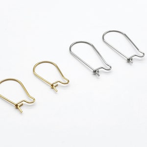 Peut inclure: Quatre crochets de boucles d'oreilles, deux dorés et deux argentés, sur fond blanc. Les crochets ont une forme incurvée en goutte d'eau avec une petite boucle en bas pour fixer des breloques ou des perles. Fournitures de bijouterie.