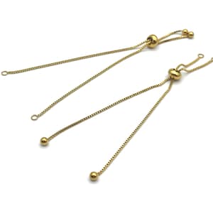 May include: Two gold-colored adjustable bracelet chains with a ball and chain design. Each chain has a small ball at the end of the chain and a larger ball in the middle. The chains are on a white background.