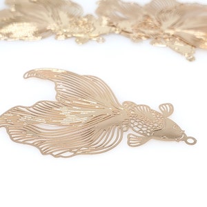 Könnte beinhalten: Goldener Metallausschnitt eines Fisches mit detailliertem Design. Der Fisch hat einen langen Schwanz und einen kleinen Kopf mit einem runden Auge.