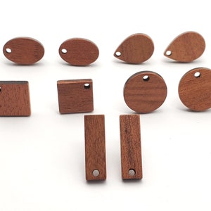 Peut inclure: Assortiment de formes en bois avec des trous pour la suspension. Les formes comprennent des cercles, des ovales, des carrés, des rectangles et des formes de larme. Le bois est de couleur brun rougeâtre.