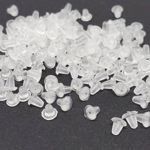 May include: A large pile of clear plastic earring backs. The backs are small and have a rounded top and a pointed bottom.