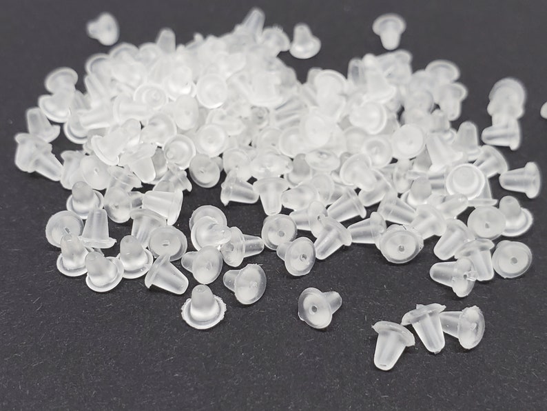 May include: A large pile of clear plastic earring backs. The backs are small and have a rounded top and a pointed bottom.