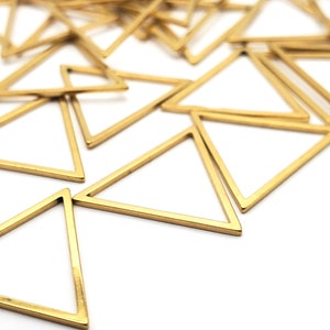 May include: A pile of gold-colored metal triangle shapes. The triangles are open and have a smooth, shiny finish.