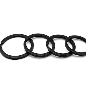 May include: A set of four circular black metal split rings arranged in a horizontal row, decreasing in size from left to right. Each ring features a double-layered coil design, providing a secure closure for organizing keys or various attachments.