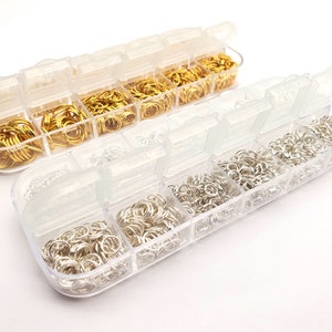 Könnte beinhalten: Zwei transparente Kunststoff-Aufbewahrungsbehälter gefüllt mit kleinen goldenen und silbernen Sprungringen. Die Behälter haben mehrere Fächer.