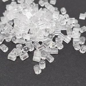 May include: A large pile of clear plastic earring backs. The backs are small and have a star-shaped design.