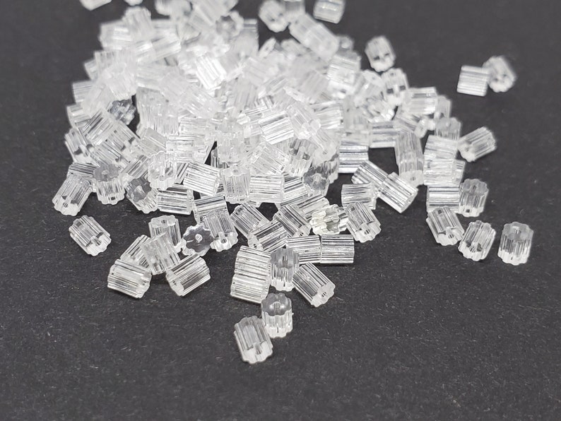 May include: A large pile of clear plastic earring backs. The backs are small and have a star-shaped design.