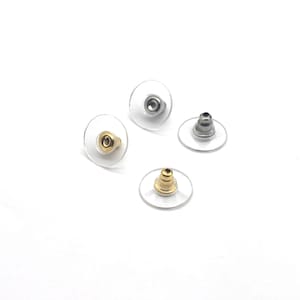 May include: Four earring backs are displayed against a white background. Two are gold-toned, and two are silver-toned. All have a clear, round, plastic disc backing.