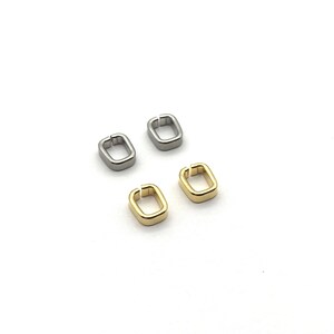 May include: Four small, rectangular metal clasps in silver and gold against a white backdrop. The clasps are open on one side, suggesting they are designed to connect two pieces. The image shows a close-up view.