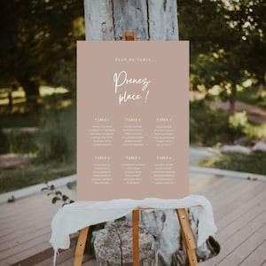 Peut inclure: Un plan de table de couleur beige clair avec le texte "Plan de Table" et "Prenez place !" en écriture blanche. Le tableau liste six tables avec les noms des invités pour une réception de mariage.